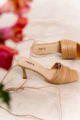 Sandalia de cuero color marrón, con tiras finas entrelazadas en el empeine y pulsera con cordón para anudar al tobillo. Tiene taco medio tipo carrete y punta cuadrada.