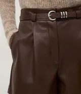Short de poliuretano color negro, de corte recto con pinzas frontales y largo corto. Incluye un cinturón fino con hebilla y pasantes metálicos.