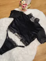 Conjunto de lencería compuesto por un top de cuello alto y una tanga, confeccionados en terciopelo negro con detalles de encaje y microtul. El top presenta mangas cortas con terminaciones en encaje y el borde inferior decorado con una cinta y encaje. La tanga es regulable y combina la textura del terciopelo con bordes de encaje.