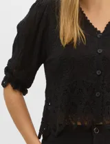 Blusa de algodón semitransparente con diseño floral bordado a tono. Presenta escote en V, cierre frontal con botones y mangas al codo ligeramente abullonadas. Incluye detalles de encaje calado estilo macramé en los puños y en el ruedo con terminaciones en ondas.