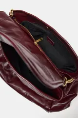 Bolso tipo shopper color borravino con diseño acolchado y pespuntes en rombos. Cuenta con solapa frontal y una correa de hombro que combina material sintético con una cadena metálica dorada.