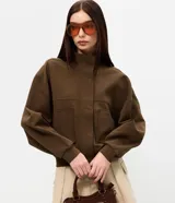 Campera marrón estilo bomber, confeccionada en punto roma, con cuello alto, mangas largas, cierre frontal oculto, bolsillos frontales aplicados y recortes en el pecho.