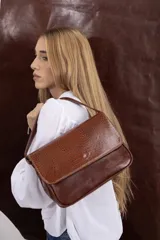 Cartera bandolera de cuero vacuno color bordó, con solapa frontal de textura símil cocodrilo y detalles de costuras pespunteadas en blanco. Cuenta con correa ajustable y cierre superior.