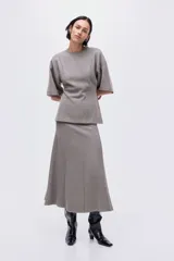 Top de punto fino color gris, con cuello redondo, hombros caídos, mangas al codo y costuras decorativas verticales en el frente que le dan un bajo levemente acampanado.
