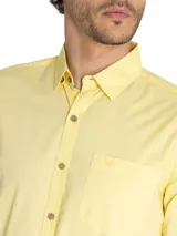 Camisa de manga larga de algodón orgánico color amarillo, con cuello abotonado, cierre frontal de botones, bolsillo en el pecho con logo bordado y mangas ajustables.