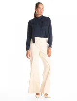 Blusa satinada de cuello alto con frunces, detalle de lazo lateral y cierre de botones. Presenta mangas largas estilo balloon con puños ajustados.