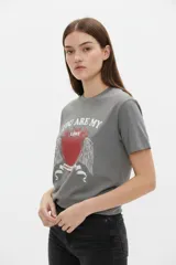 Remera de algodón negra de manga corta y cuello redondo, con estampa frontal que incluye letras rojas y gráficos en tonos dorados.
