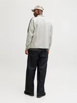 Buzo de manga larga color gris melange, con cuello tipo polo y ajuste holgado. Presenta estampado gráfico frontal con tipografía y detalles en negro, además de bandas laterales en las mangas.