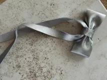 Moña de cuero color marrón con forma de lazo y tiras colgantes.