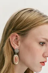 Pendientes colgantes con base tipo botón circular cubierta de brillos oscuros y pieza central ovalada en tonos beige y rosado, elaborada en resina.