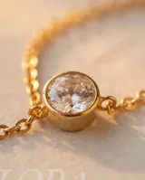 Collar estilo corbatero de acero dorado con dos circonias engarzadas en formato circular, una en el centro y otra en el extremo inferior.