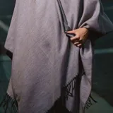 Poncho de acrílico color gris con flecos en el borde inferior.