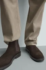 Bota estilo Chelsea con parte superior de piel con acabado en serraje, elásticos laterales para facilitar el calce, horma redonda y suela con ligero tacón.