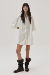 Vestido corto color crudo con rayas verticales plateadas, de manga larga abullonada y abotonado desde el escote hasta el bajo.