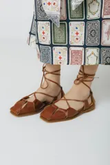 Sandalias bajas de cuero color marrón con tiras que se atan al tobillo.