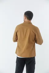 Sobrecamisa de jean color tostado, con cuello clásico, cierre frontal con botones y dos bolsillos frontales con solapa. Presenta mangas largas con puños abotonados y un pequeño parche decorativo en el ruedo.