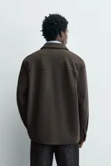 Sobrecamisa relaxed fit color beige con tejido elástico, cuello solapa, manga larga con puños abotonados, bolsillos de plastrón con solapa en el pecho, bolsillos laterales de vivo en la cadera y cierre frontal de botones.