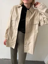 Sobrecamisa negra de ecocuero con cuello clásico, cierre frontal con botones, mangas largas y bolsillos de parche en el pecho.