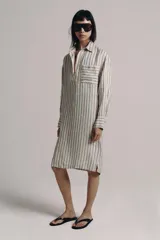 Vestido midi estilo camisero de Zara Woman Collection, confeccionado en lino, con estampado de rayas verticales azules sobre fondo beige. Cuenta con cuello solapa, escote en V con botonadura parcial, manga larga con puños abotonados, un bolsillo de plastrón en el pecho y bajo redondeado.