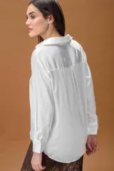 Camisa blanca de corte clásico y diseño holgado, con cuello camisero, cierre frontal de botones y mangas largas con puños anchos.