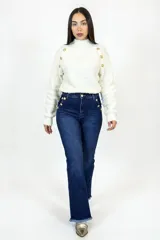 Pantalón de jean azul oscuro de corte flare con tiro alto. Presenta detalles de botones dorados en los laterales de la cintura y ruedo deshilachado.