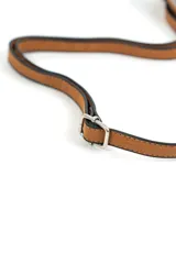 Cartera bandolera marrón decorada con tachas metálicas plateadas en los laterales y en dos líneas verticales frontales, con correa ajustable y cierre superior.