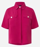 Camisa color fucsia de tejido airflow, con cuello camisero, mangas cortas con pliegues, cierre frontal con botones metalizados y bolsillos con solapa en el pecho.