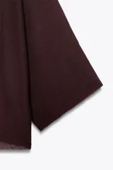 Jersey de punto color vino tinto, de corte amplio y holgado, con cuello bote y un detalle de capa asimétrica superpuesta en la parte superior delantera. Mangas anchas tipo murciélago.