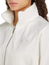 Cortavientos blanco de corte regular, con cuello alto, cierre de cremallera, dos bolsillos con botones, detalles distintivos de Tommy Hilfiger y logo gráfico bordado en el pecho.