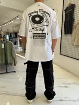 Remera oversize blanca de manga corta, con gran estampado en la espalda de una bandeja de vinilos y texto temático musical.