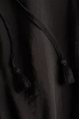 Vestido corto negro de mezcla de viscosa, con escote redondo, abertura frontal con tiras finas y mangas largas abullonadas con puños elásticos. Presenta sección entallada en la cadera con alforzas y falda corta con volados escalonados.