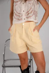 Short blanco de tiro alto con pliegues frontales y cierre de botón metálico.