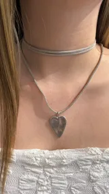 Gargantilla doble compuesta por un choker de gamuza fina y un collar de cadena plana tipo serpiente con un dije de corazón plateado.