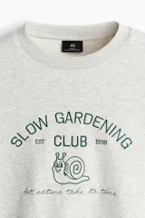 Buzo de cuello redondo en mezcla de algodón color gris melange, con diseño bordado frontal que incluye texto y el dibujo de un caracol.