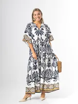 Maxi vestido blanco con estampado paisley en azul marino y detalles en tonos dorados, con cuello en V, mangas amplias y diseño escalonado.