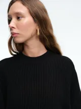 Sweater de tejido de punto acanalado en color blanco, con cuello redondo, mangas largas y corte holgado. Presenta un diseño minimalista y contemporáneo.