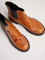 Bota tipo chelsea de cuero con textura de reptil, color suela. Presenta paneles elásticos laterales en color negro, suela de goma dentada con pespuntes en contraste y puntera redondeada.