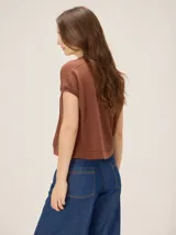 Remera tejida color beige de corte relajado, con mangas cortas y detalle de costuras frontales marcadas. Incluye un pequeño bordado distintivo en el borde inferior.