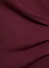 Vestido midi de color bordó, sin mangas, con cuello redondo y diseño entallado. Presenta un detalle de fruncido lateral en la cintura y cierre posterior.
