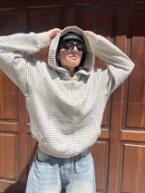 Campera con capucha y cierre frontal, color hueso con rayas horizontales finas en gris oscuro.