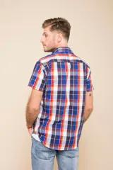 Camisa de manga corta con estampado de cuadros en tonos verdes, azules y blancos. Presenta cuello clásico, cierre frontal con botones y dos bolsillos delanteros con solapa.