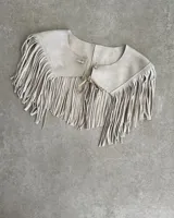 Pechera de cuero vacuno color beige, con diseño de cuello y flecos largos en todo el borde inferior. Se ajusta al frente con un lazo de cuero.
