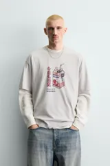 Camiseta relaxed fit color beige con cuello redondo y manga corta. Presenta un estampado frontal de un cartón de leche de fresa con una pajita, texto en japonés y la frase "SWEET MOMENTS".