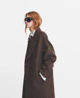 Abrigo de corte sastre con diseño de doble botonadura y solapas amplias. Presenta un estampado de cuadros pequeños en tonos marrones y oscuros, con una silueta estructurada y elegante.