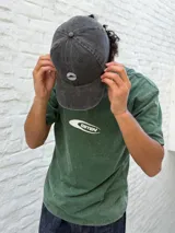 Remera de manga corta color verde oscuro con efecto acid wash y un logo ovalado blanco con el texto "OSTEN" en el centro del pecho.