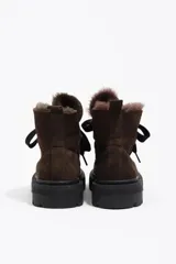 Botín de caña baja confeccionado en gamuza color marrón oscuro, con interior forrado en pelo sintético. Presenta cierre mediante cordones frontales, puntera redonda y suela de goma dentada en color negro.