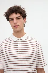 Remera polo de manga corta con diseño a rayas horizontales marrones sobre base blanca, cuello camisero en color blanco con media cartera de botones y aberturas laterales en el dobladillo.