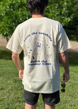 Remera color arena de corte recto con estampado en la espalda que incluye un vaso con cara, estrellas y las frases "Taste the sunshine" y "Catch the summer vibes".