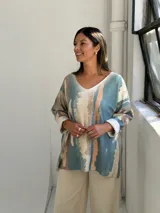 Sweater de punto con diseño abstracto de rayas verticales en tonos petróleo, beige y terracota. Presenta escote en V, corte holgado y mangas largas con puños vueltos.