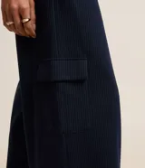 Pantalón recto de cintura baja, confeccionado en punto roma con rayas verticales en hilo teñido. Presenta trabillas en la cintura, cierre tradicional, pliegues, bolsillos cargo laterales y bolsillos falsos atrás.